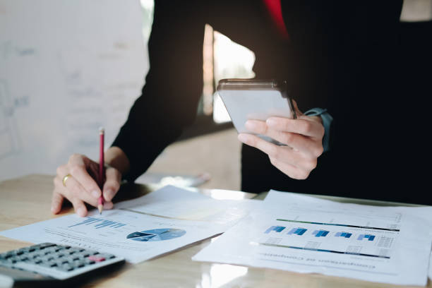istock Businesswoman pen pointing graph chart in this mount and use mobile phone for Plans to improve quality next month. 1143306514