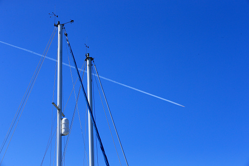 Yacht masts with the power of a jet stream from an airliner crossing in the blue sky . Mast rigging shines in the sunlight photo all about straight lines in a creative view.