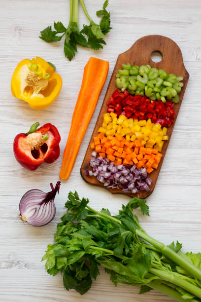 istock Chopped fresh vegetables (carrot, celery, red onion, red and yellow peppers) arranged on cutting board over white wooden background, top view. Overhead, from above, flat lay. 1143316686
