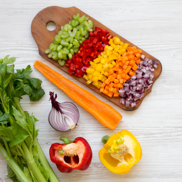 istock Chopped fresh vegetables (carrot, celery, red onion, red and yellow peppers) arranged on cutting board on a white wooden surface, view from above. Flat lay, overhead, top view. 1143317370
