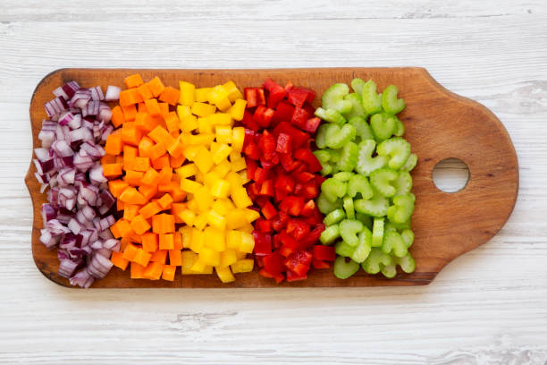 istock Overhead view, chopped fresh vegetables (carrot, celery, red onion, colored peppers) arranged on cutting board on a white wooden surface. Flat lay, from above, top view. 1143317373