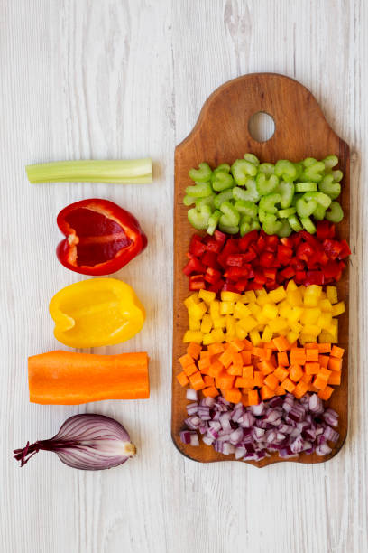istock Chopped fresh vegetables (carrot, celery, onion, colored peppers) arranged on cutting board on a white wooden surface, top view. Overhead, from above. 1143317531