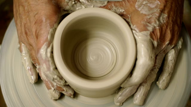 man makes a jug with dirty arms on a Potter's wheel from raw wet clay