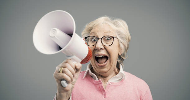 istock Cheerful senior lady shouting into a megaphone 1143332201