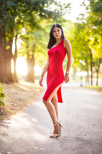 Young woman in red dress is posing in public park