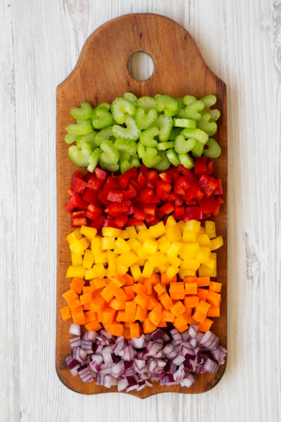 istock Chopped fresh vegetables (carrot, celery, red onion, colored peppers) arranged on cutting board on a white wooden background. Flat lay, from above, top view. 1143338849