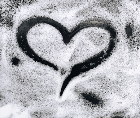 Heart shape on soap foam on black background. Car wash.