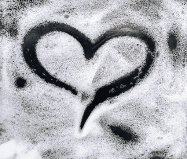 Photo of Heart shape on soap foam on black background.