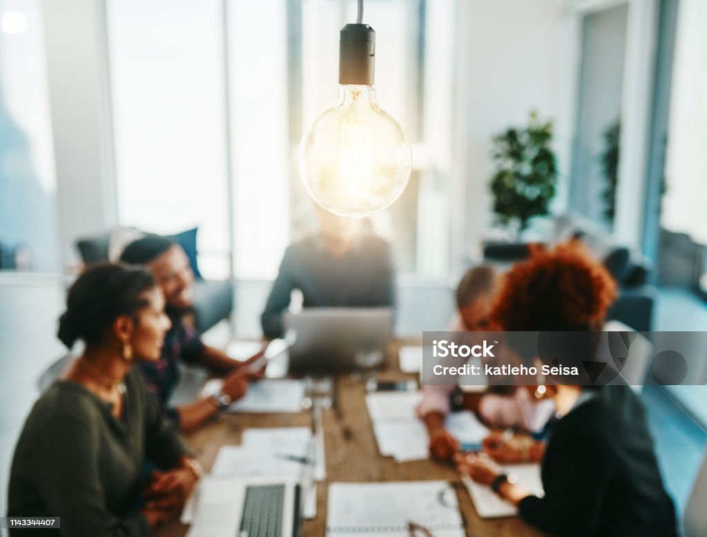 You're one meeting away from a brilliant idea Shot of a group of young businesspeople having a meeting with a lightbulb in the foreground Innovation Stock Photo