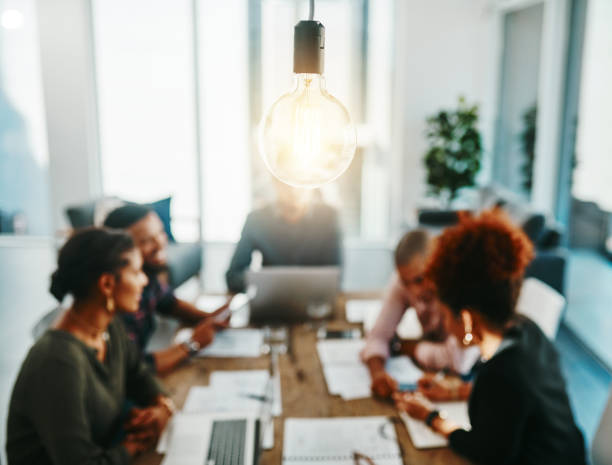 You're one meeting away from a brilliant idea Shot of a group of young businesspeople having a meeting with a lightbulb in the foreground resourceful stock pictures, royalty-free photos & images