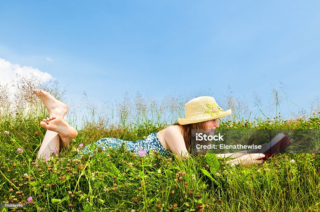 Chica joven leyendo libro en prado - Foto de stock de Acostado libre de derechos