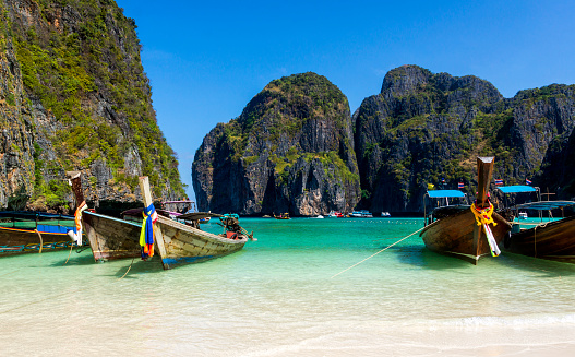 Long-tail boats on a Maya Bay sandy beach, surrounded by tall mountains with green trees, Phi Phi Lay island, Thailand