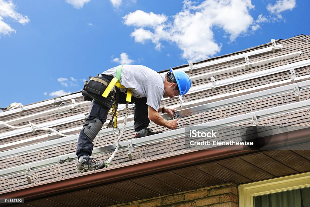 Uomo che lavora sul tetto, l'installazione di rails per pannelli solari - Foto stock royalty-free di Costruttore di tetti