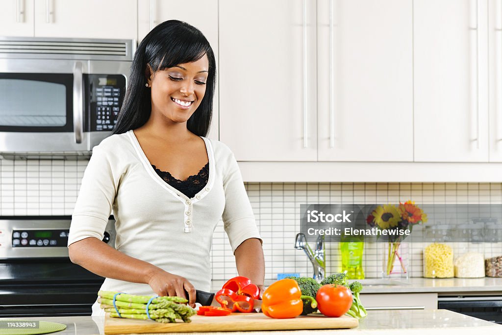 A young woman cutting vegetables in a kitchen Smiling black woman cutting vegetables in modern kitchen interior Cooking Stock Photo