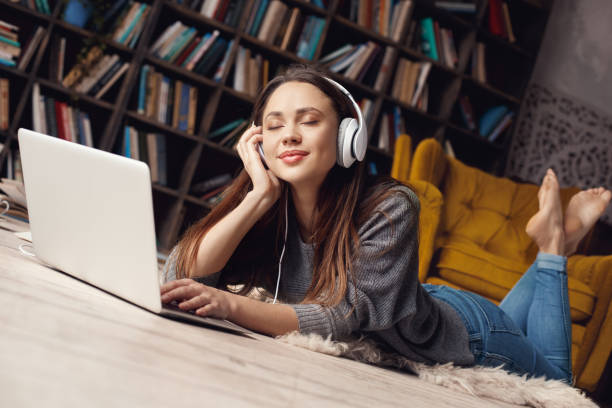 自宅�で図書館の若い女性学生は、お気に入りの曲を聴いて横たわっている - armchair comfortable relaxation headphones ストックフォトと画像