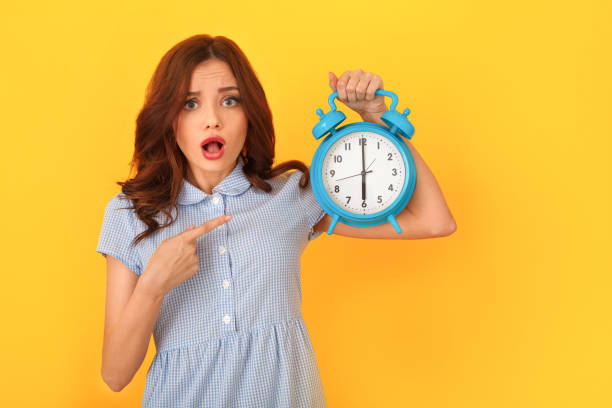 istock Young woman studio isolated on yellow holding alarm clock pointing at time 1143390304
