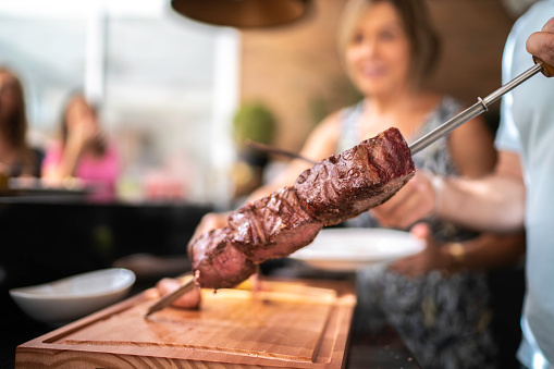 Focus on man's hand cutting picanha meat during barbecue