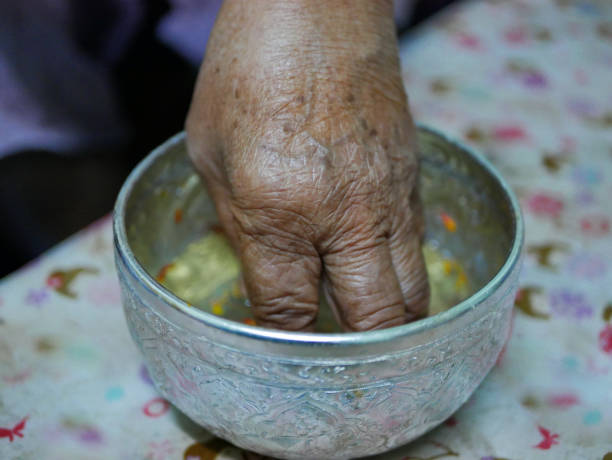 Selective focus of a hand of elderly person dipping into a cup ( salung ) filled with holy turmeric water before spraying the blessing water during Rod Nam Dam Hua ceremony, paying respect to the elders, in Songkran festival in Thailand enfoque selectivo de una mano de persona de edad avanzada sumergiendo en una taza (salung) llena de agua de la cúrcuma sagrada antes de pulverizar el agua de bendición durante la ceremonia de rod nam dam hua, pagando respeto a los ancianos, en el festiva