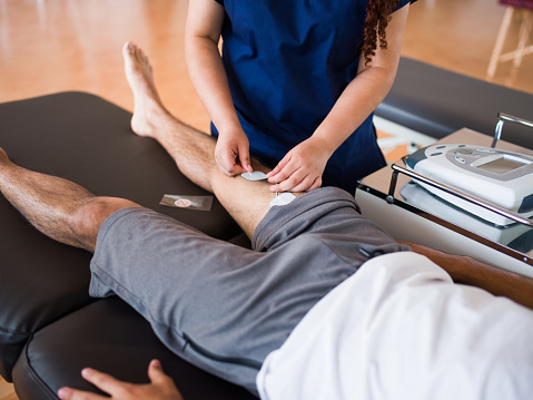 An athletic male patient lying down on a massage table and getting an alternative treatment for his leg.