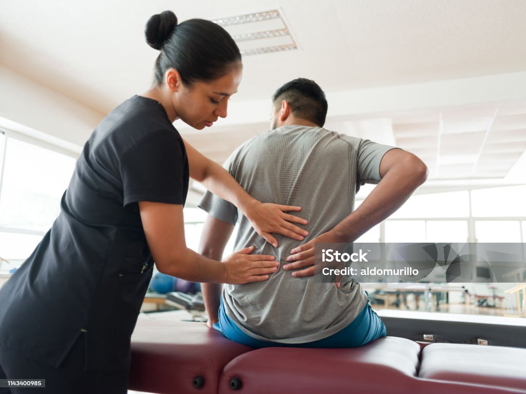 Female massage therapist massaging patient's back A female massage therapist standing behind a male patient and massaging his back with both hands. Physical Therapy Stock Photo