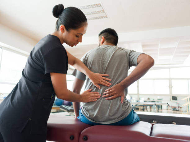 Female massage therapist massaging patient's back A female massage therapist standing behind a male patient and massaging his back with both hands. physiotherapy stock pictures, royalty-free photos & images