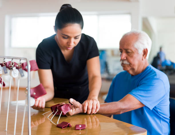 Senior patient exercising hand with physical therapy device A senior male patient sitting and exercising his hand with a physical therapy device next to a occupational therapist. occupational therapy photos stock pictures, royalty-free photos & images