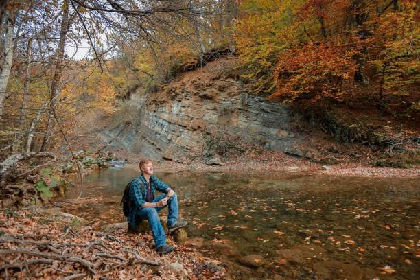 istock Man sits near mountain stream in autumn 1143416819