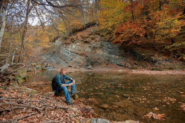 istock Man sits near mountain stream in autumn 1143416824