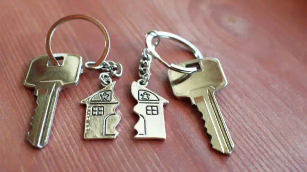 Pendant of key ring in shape of house divided in two parts on wooden background, closeup view. Dividing house when divorce, division of property and real estate.