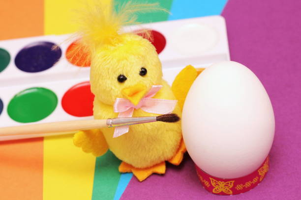 frohe ostern. gelbes spielzeughühnchen mit einem pinsel bereitet sich vor, um ein weißes hühnerei-aquarell zu malen. - baby chicken eggs young bird easter stock-fotos und bilder