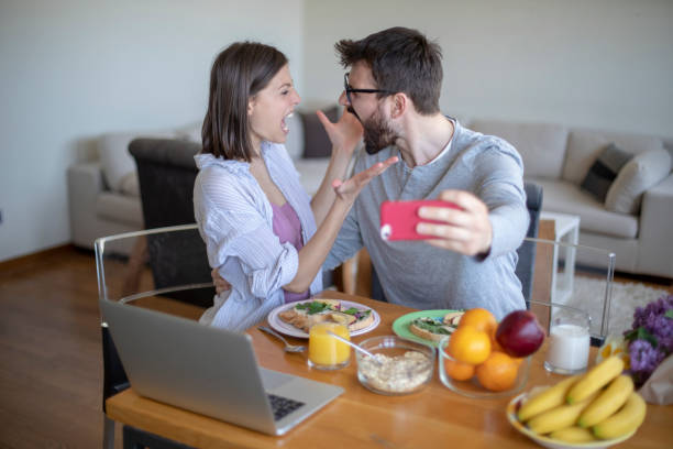 istock Young couple with vegan breakfast in dining room and computer taking selfie. 1143430260