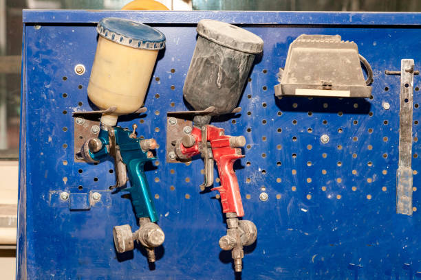istock Two body paint gun sprayer red and blue installed on a workbench in a vehicle repair workshop next to another tool and lamp. Industry in auto service 1143432620