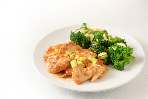 marinated chicken breast fillet with spring onions and broccoli with almond sticks as a healthy meal with little carbohydrates for slimming on a plate, background is blending to white, copy space, selected focus, narrow depth of field
