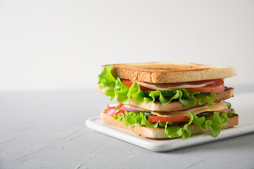 Sandwich with white toast bread, bacon, tomato, onion, salad, cheese on light background. Space for text