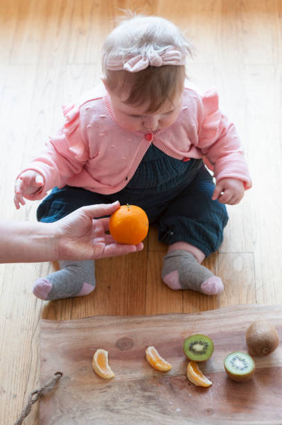 istock a hand presents a tangerine to a baby 1143456406