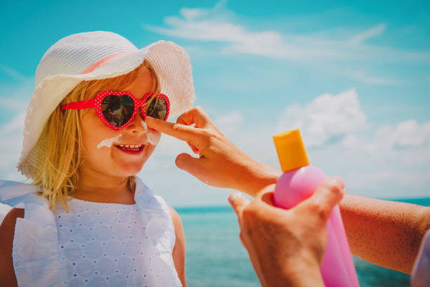 mother put sunblock cream on little daughter face at beach stock photo
