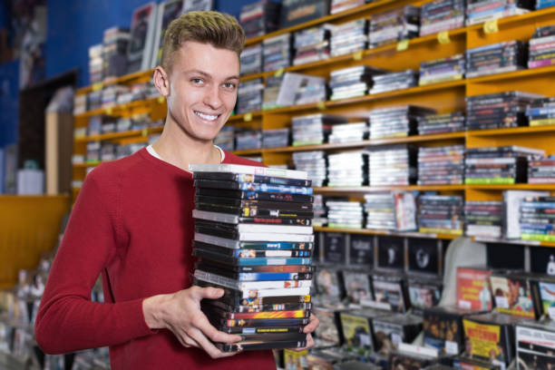 Smiling young guy customer  holding stack of DVDs in shop