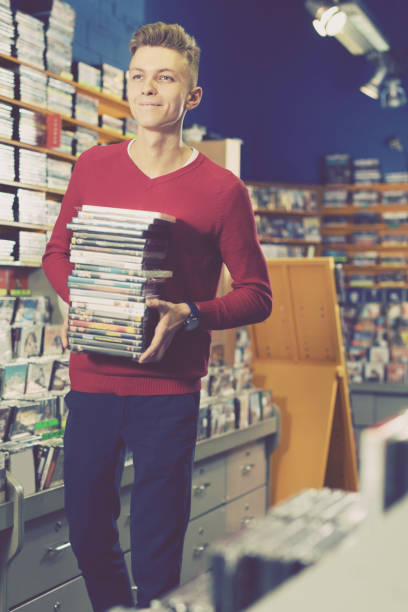 istock Happy guy standing with stack of DVDs in hands in shop 1143463088