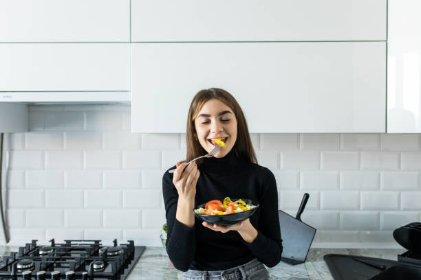 istock Smiling young woman eating a salad in her kitchen 1143463258