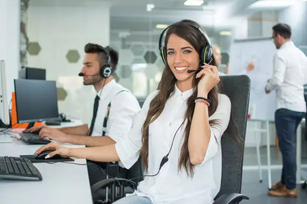 Smiling friendly female call-center agent with headset working on support hotline in the office