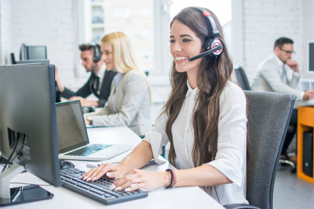 Beautiful young woman with headset working on computer while talking with client in call center. Online customer support. Beautiful young woman with headset working on computer while talking with client in call center. Online customer support. switchboard operator stock pictures, royalty-free photos & images