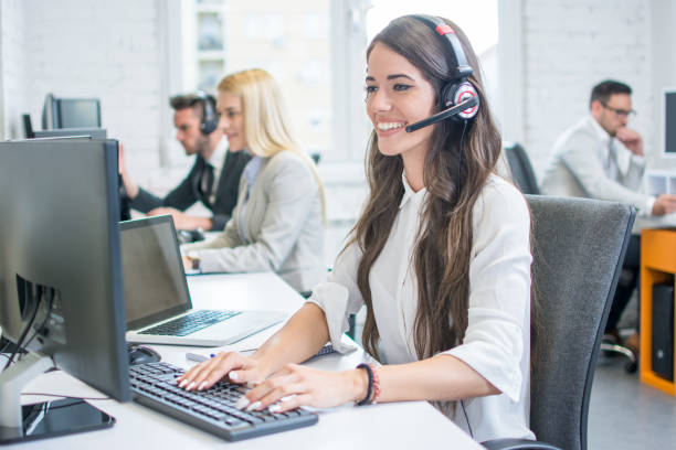 beautiful young woman with headset working on computer while talking with client in call center. online customer support. - bluetooth headset women customer imagens e fotografias de stock