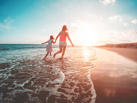 Mother and daughter running inside the water on tropical beach - Mum playing with her kid in holiday vacation next to the ocean - Family lifestyle and love concept - Focus on bodies silhouette