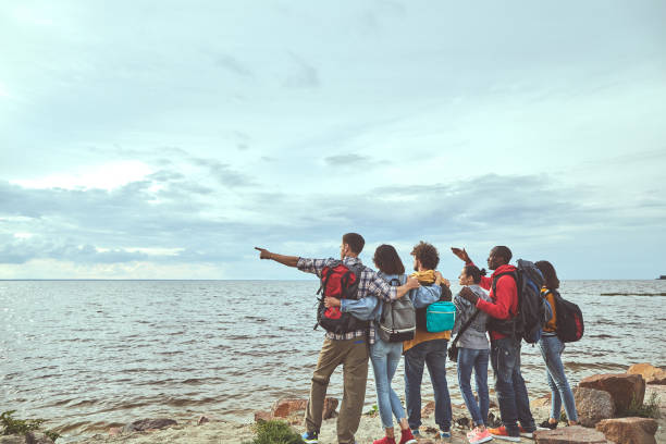 Waiting for ship. Portrait of friendly cronies looking at sea horizon. Guy pointing into the distance. Copy space on the left side