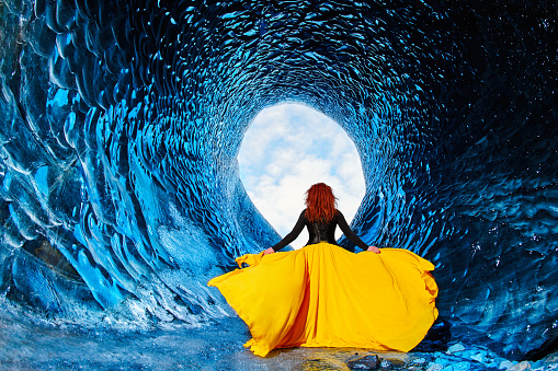 rear view of woman with flying yellow dress in ice cave walking.photo taken in Anaconda Cave, Iceland.