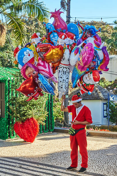 Christams Funchal, Portugal - Dezember 20, 2018: A young man dressed as Santa Claus with balloons and smartphone stands on the summery Christmas market in Funchal. funchal christmas stock pictures, royalty-free photos & images