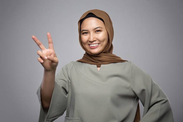 istock Beautiful Muslim girl gesturing peace sign with smiling face isolate on grey background 1143478991
