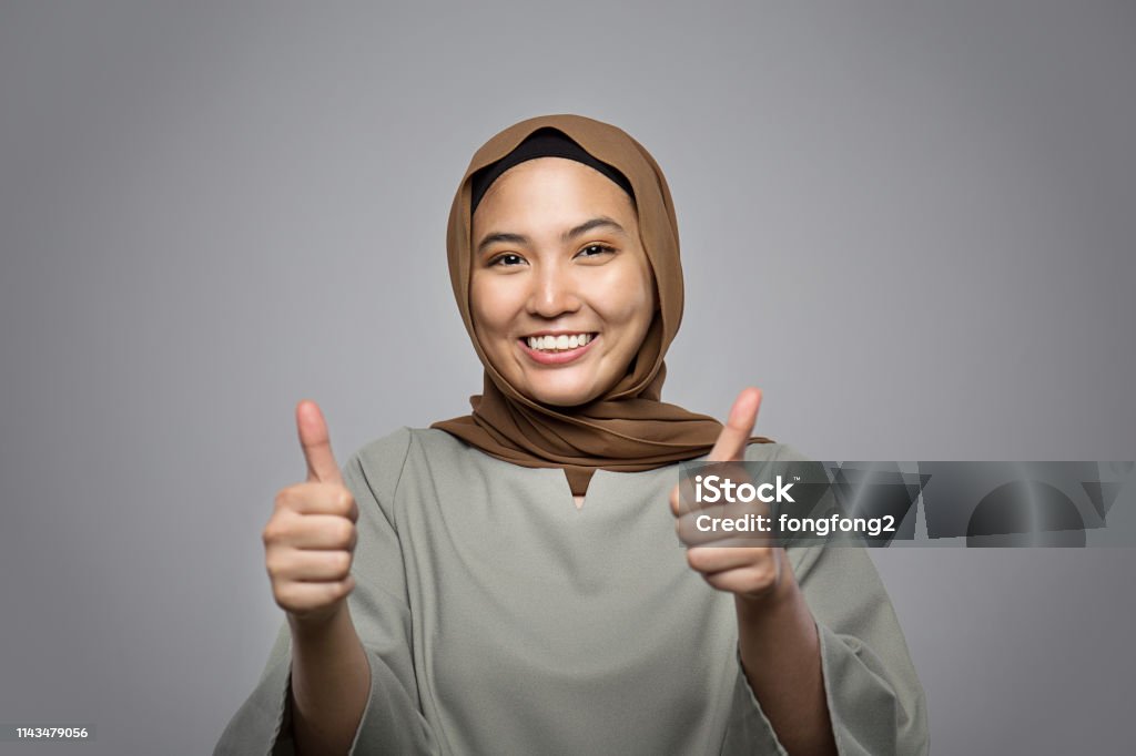 young muslim woman smiling at camera and showing thumb up isolated on grey Thumbs Up Stock Photo