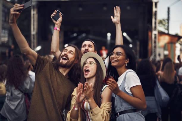 Cheerful friends making selfie at outdoor music festival Having fun. Waist up portrait of young people taking photo with smartphone while enjoying concert group of people wearing eyeglasses stock pictures, royalty-free photos & images