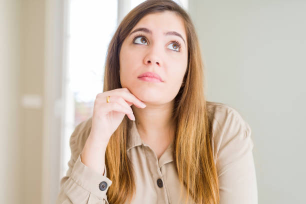 istock Beautiful young woman at home with hand on chin thinking about question, pensive expression. Smiling with thoughtful face. Doubt concept. 1143481206
